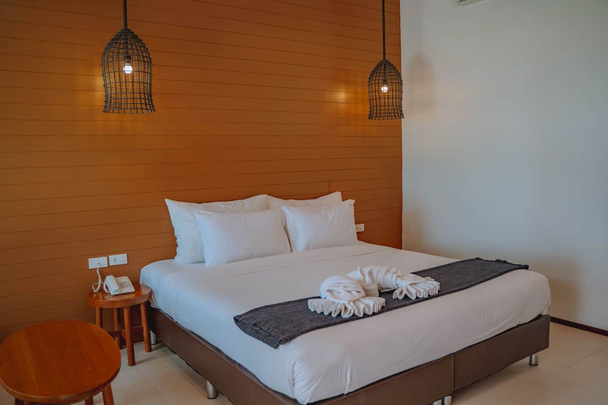 A neatly made bed with white linens and a towel arrangement, a bedside table with a phone, and two hanging pendant lights.
