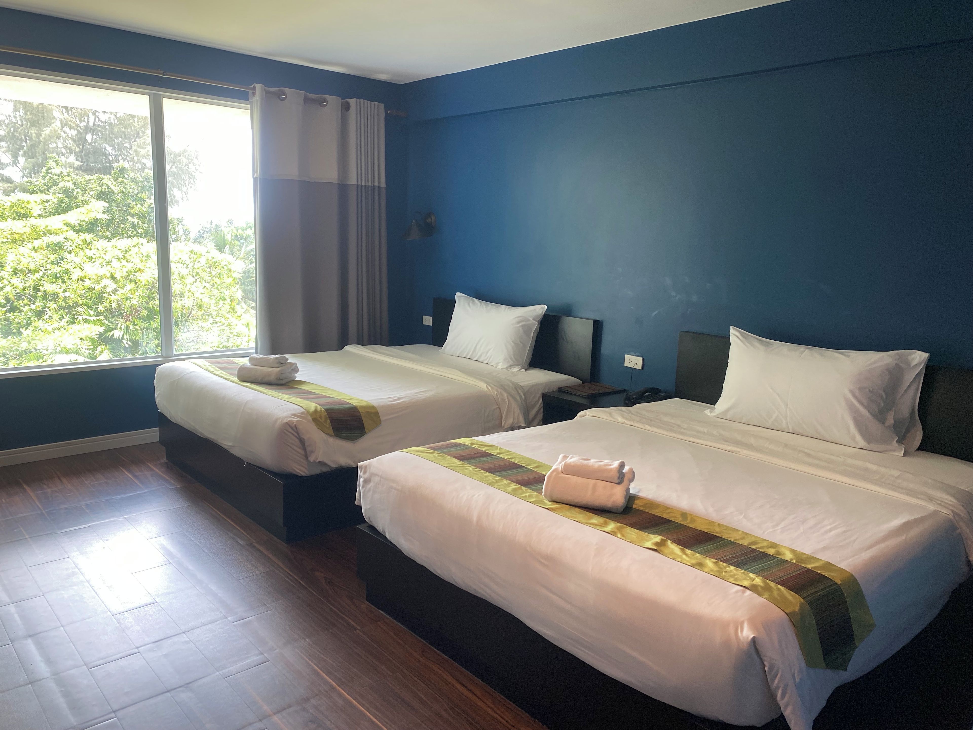 A hotel room with two beds, a large window, and a view of greenery outside.