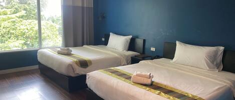A hotel room with two beds, a large window, and a view of greenery outside.