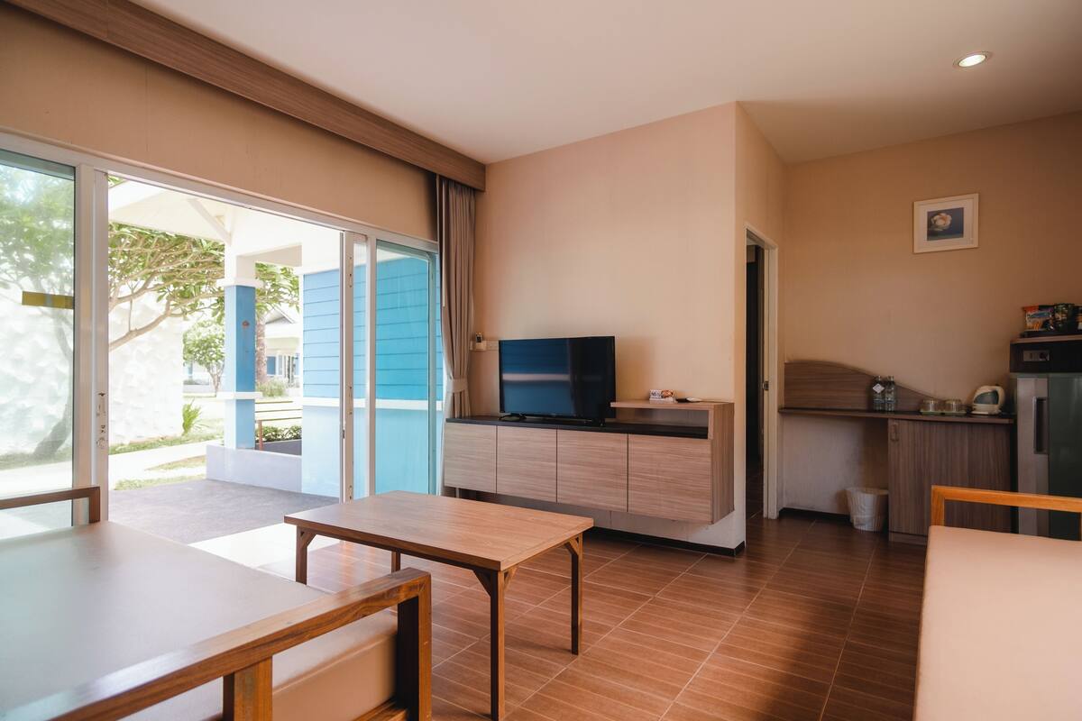 A modern room with a dining table, a TV on a cabinet, a kitchen area, and a sliding glass door leading to an outdoor area.