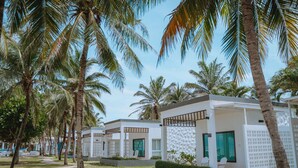 Une rangée de villas modernes aux façades blanches et aux portes vertes, entourées de palmiers et surplombées par un ciel d’un bleu limpide.