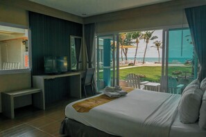 Een hotelkamer met een bed, een bureau, een televisie en uitzicht op het strand.