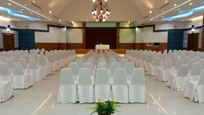 A conference room with rows of white chairs and a stage at the front.