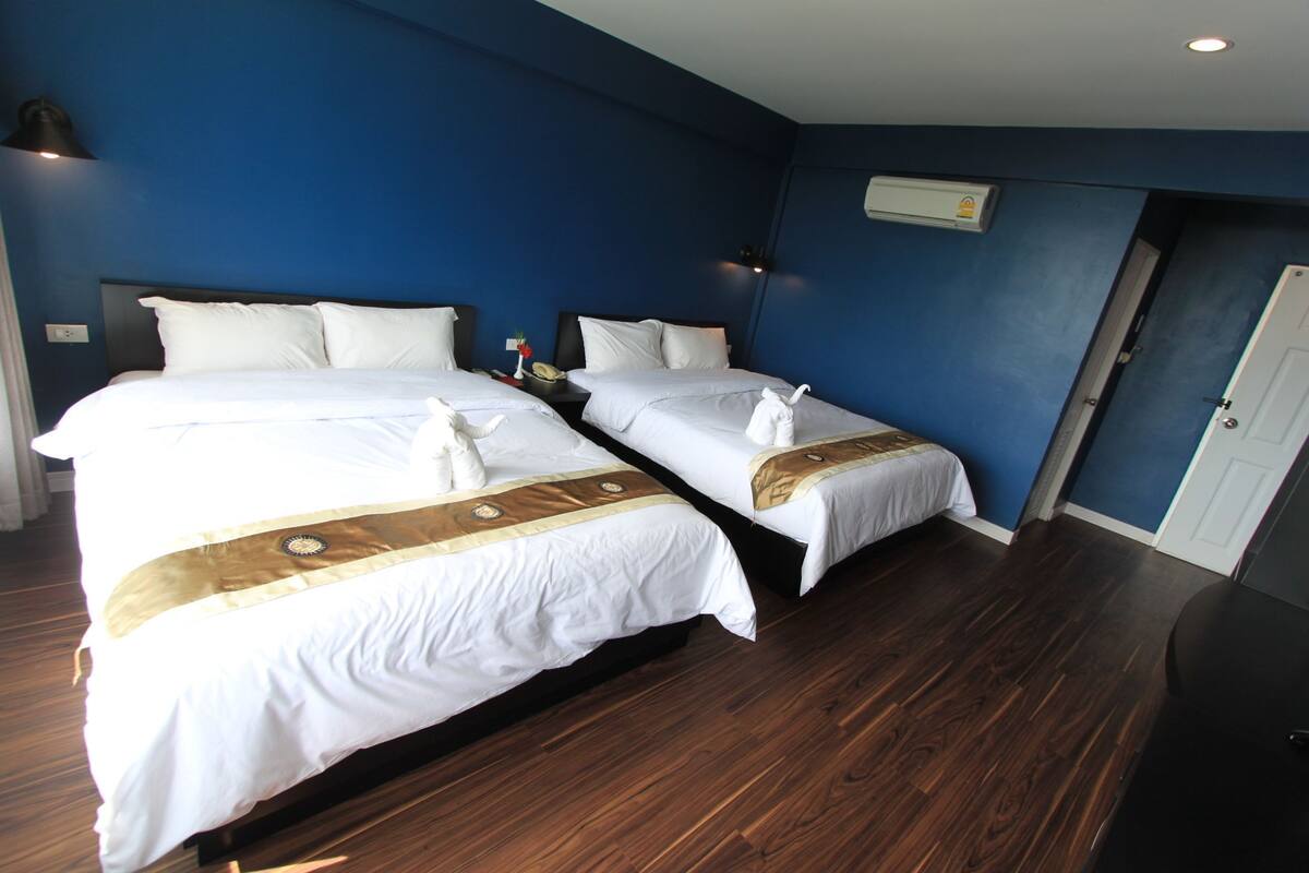 A hotel room with two beds, a wooden floor, a blue wall, and a white door.