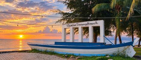 A boat named 'Chao Tao Tosang Beach' docked at a beach with a sunset in the background.