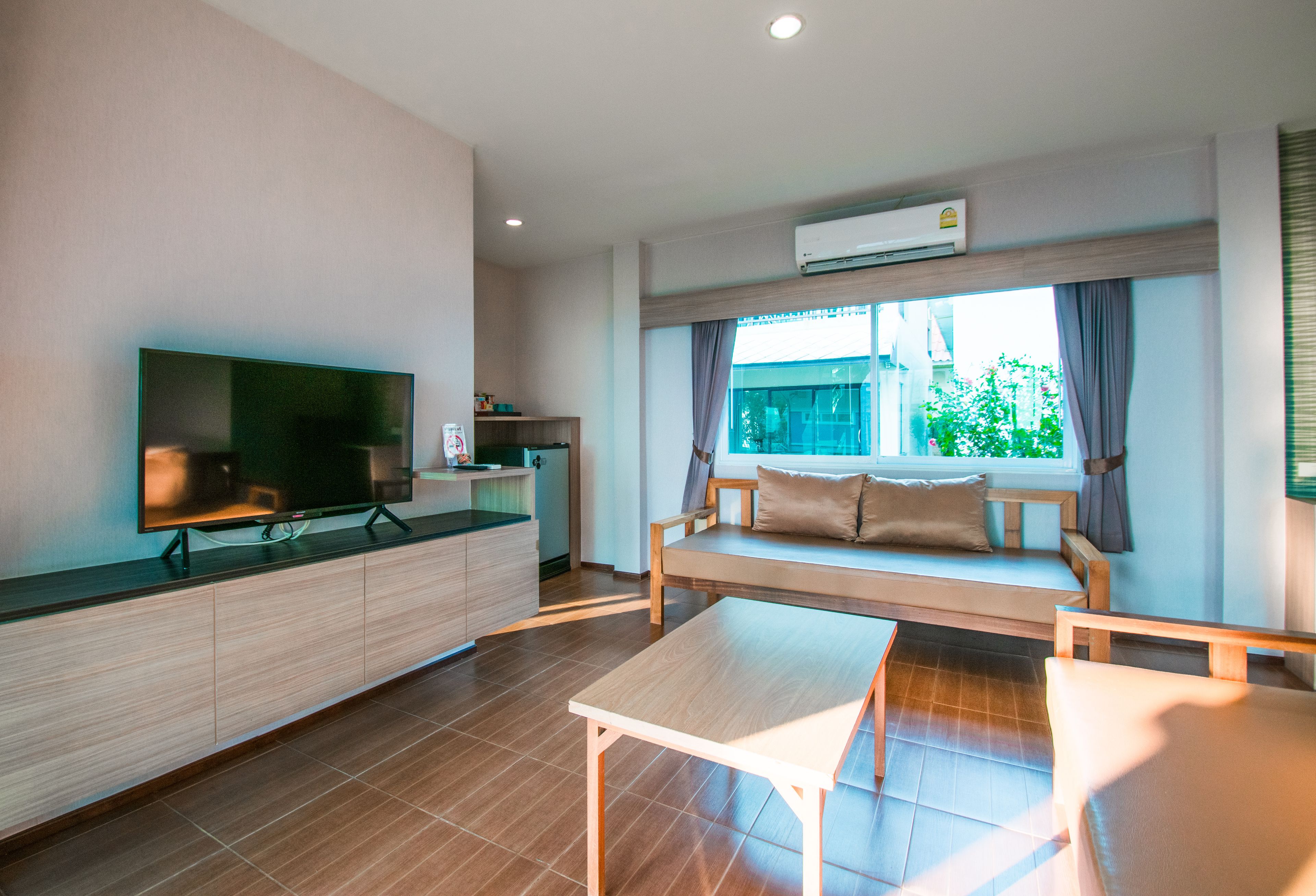 A modern living room with a flat-screen TV, a wooden bench, a small table, and a kitchen area with a refrigerator.
