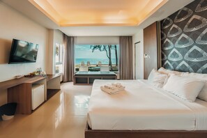 A hotel room with a bed, a TV, a desk, and a view of the beach.