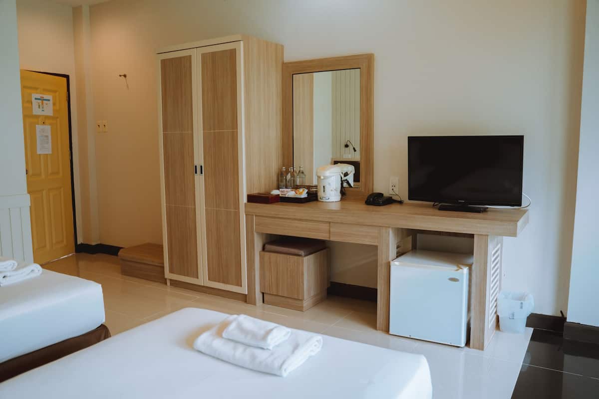 A hotel room with two beds, a wooden wardrobe, a desk with a television, a coffee maker, and a small refrigerator.