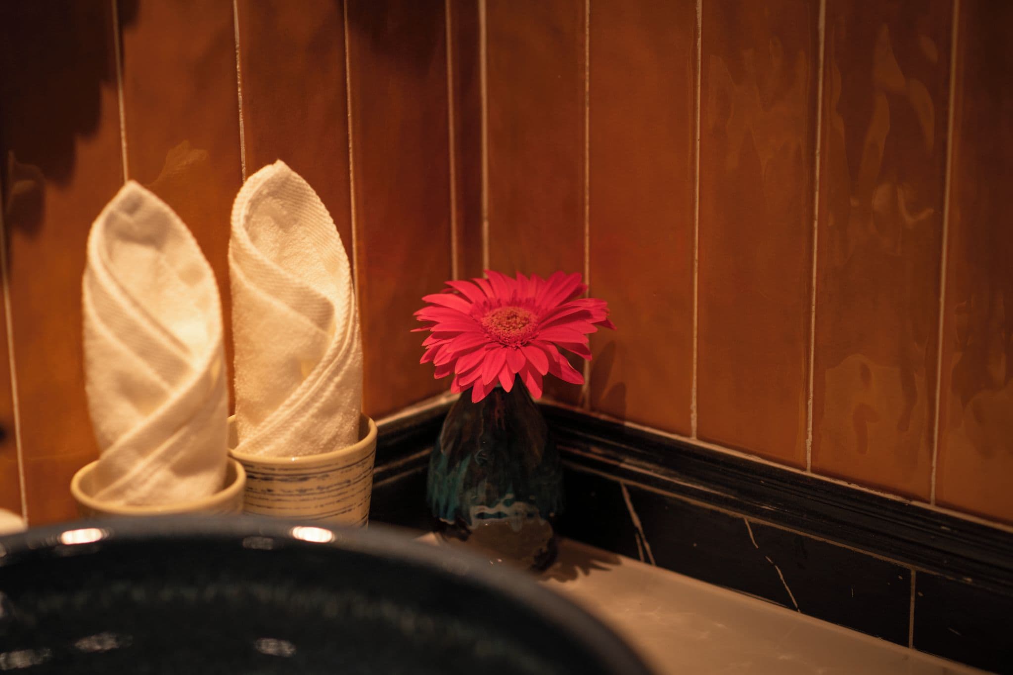A room with a wooden wall and a vase with a red flower.