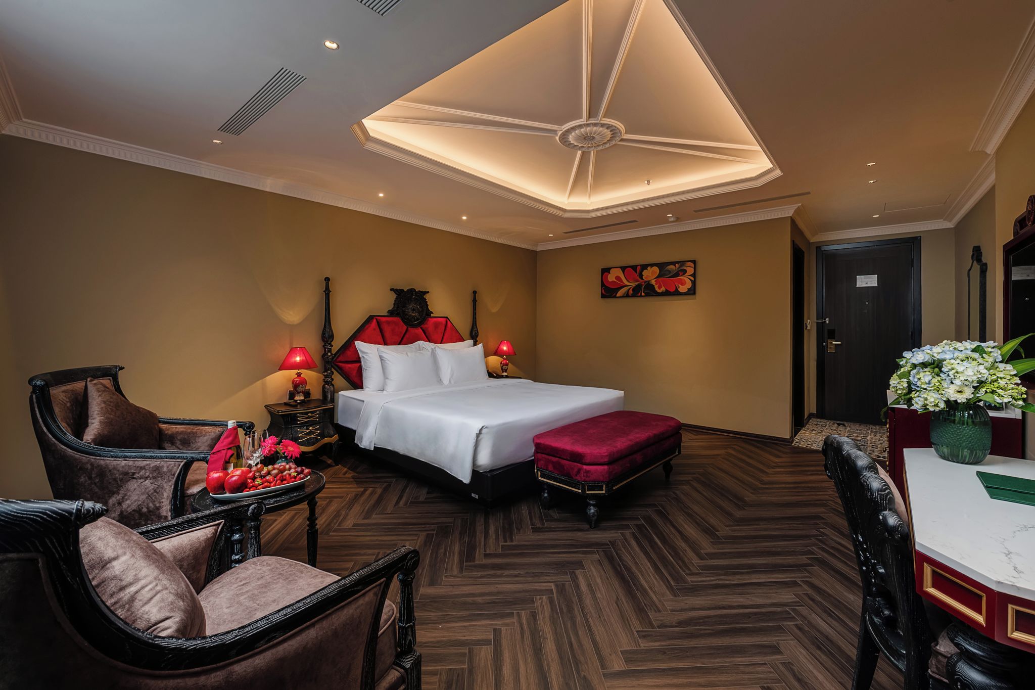 Ein Hotelzimmer mit einem großen Bett, einer Sitzecke mit Sessel und Tisch sowie einer dekorativen Deckenleuchte.