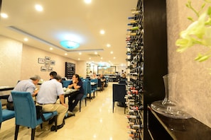 Um restaurante com mesas, cadeiras, uma estante para vinhos e um quadro de cardápio.