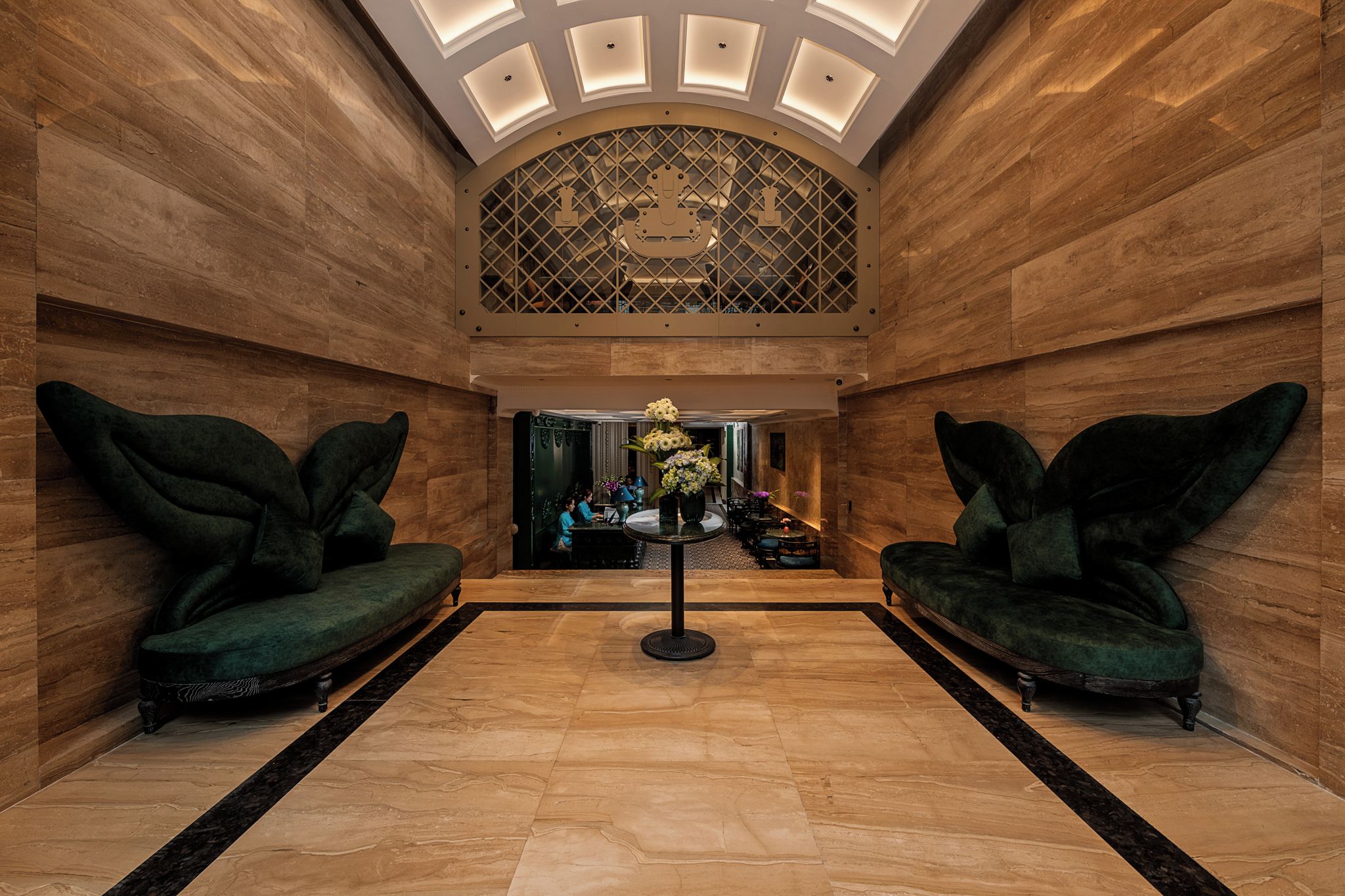 Eine Lobby mit zwei grünen Sofas, einem zentralen Tisch mit Blumen und einer gemusterten Decke.
