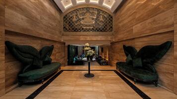 Eine Lobby mit zwei grünen Sofas, einem zentralen Tisch mit Blumen und einer gemusterten Decke.