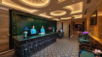 A reception area with a marble counter, two receptionists, and a decorative ceiling.