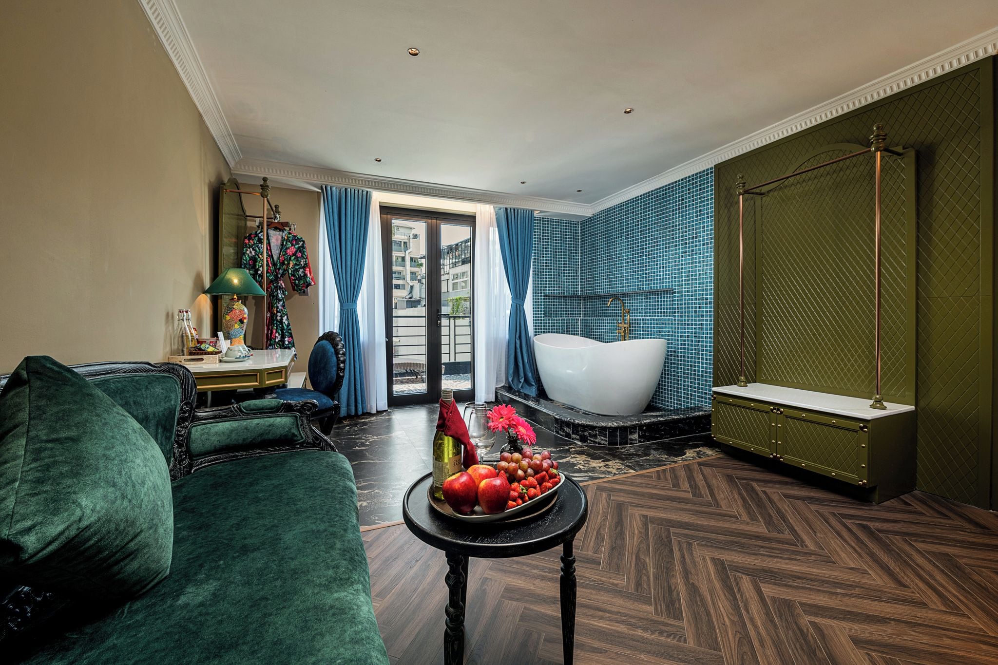 Un salon moderne avec un canapé vert, une table ronde sur laquelle sont disposés des fruits, une grande fenêtre et une salle de bain avec une baignoire.