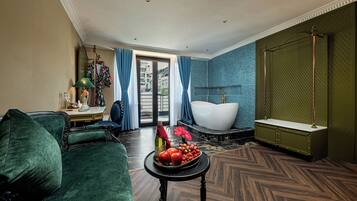 Een moderne woonkamer met een groene bank, een ronde tafel met fruit, een groot raam en een badkamer met een bad.