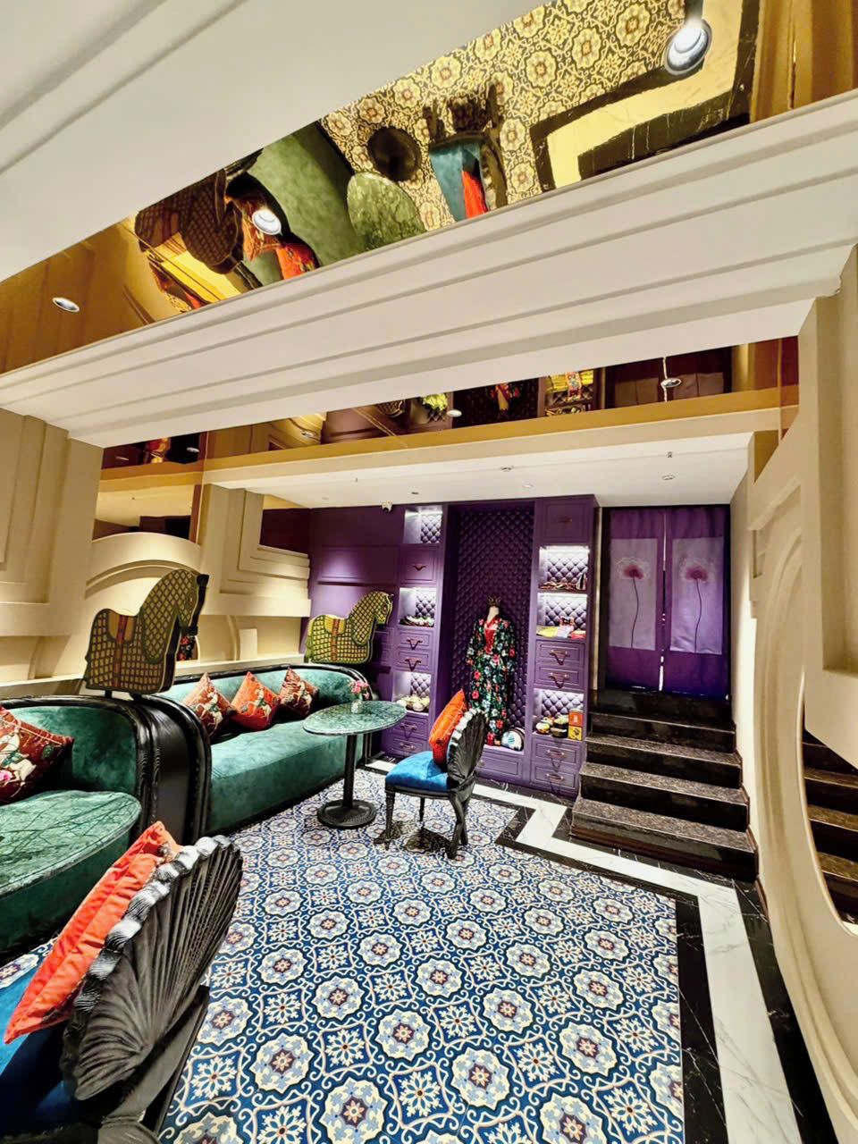 A spacious lobby with a patterned floor, a staircase, and a seating area with a sofa and armchairs.