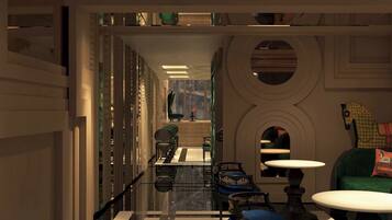 A corridor with a reflective floor, a seating area with blue upholstered chairs, and a table with a white top.