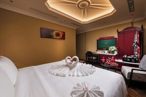 Quarto de hotel com cama, escrivaninha, cadeira e televisão.