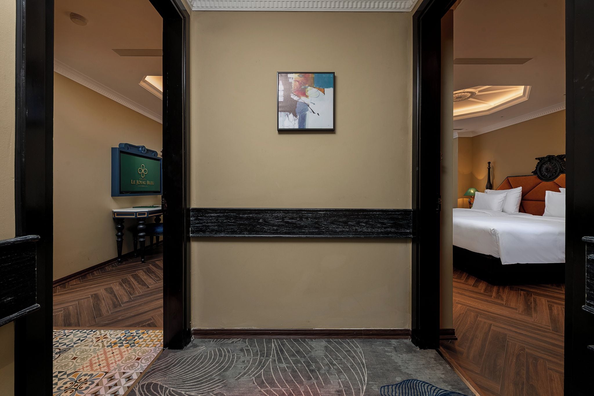 A hotel hallway leading to a bedroom with a bed, a painting on the wall, and a television in the corner.
