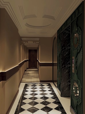 A hallway with a checkered floor, a wooden door at the end, and a wall with a decorative panel. - Hôtel Le Joyau Bleu Hanoï (Hanoi)