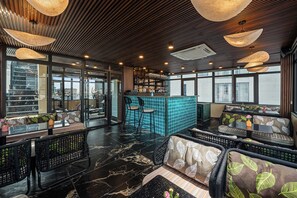 A modern interior with seating areas, a bar, and large windows. - Hôtel Le Joyau Bleu Hanoï (Hanoi)