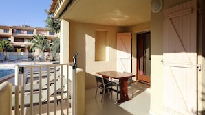 A balcony with a pool, a table, and chairs, and a view of a building with balconies and palm trees. - Résidence Lago Verde (Porto-Vecchio)