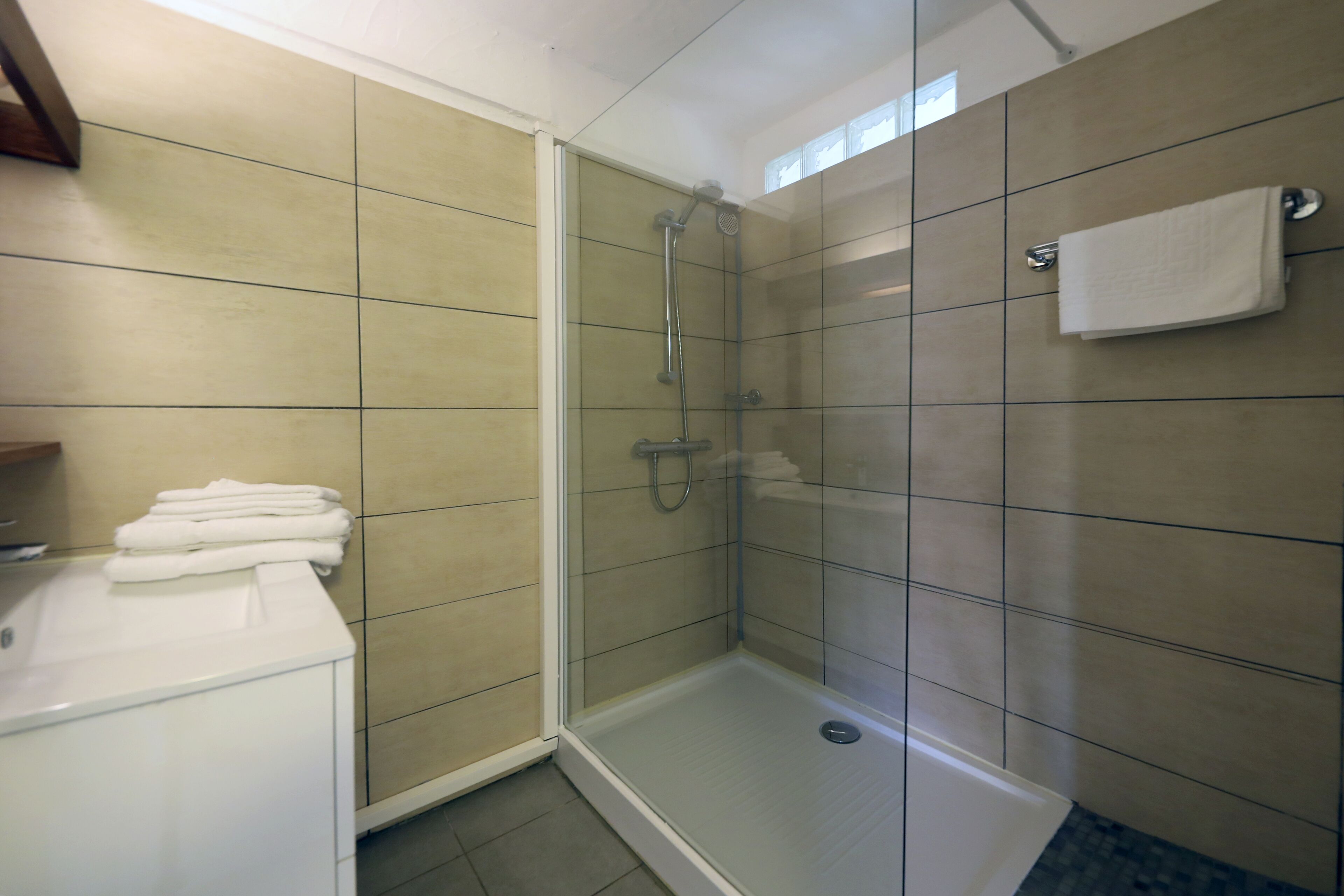 Une douche fermée par des parois de verre, avec un porte-serviettes blanc et une pile de serviettes pliées posée sur un meuble blanc.