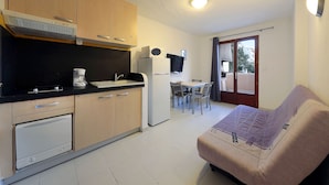 A compact kitchen with a built-in oven, a refrigerator, and a microwave. There is a dining area with a table and chairs, and a sofa in the living area. - Résidence Lago Verde (Porto-Vecchio)