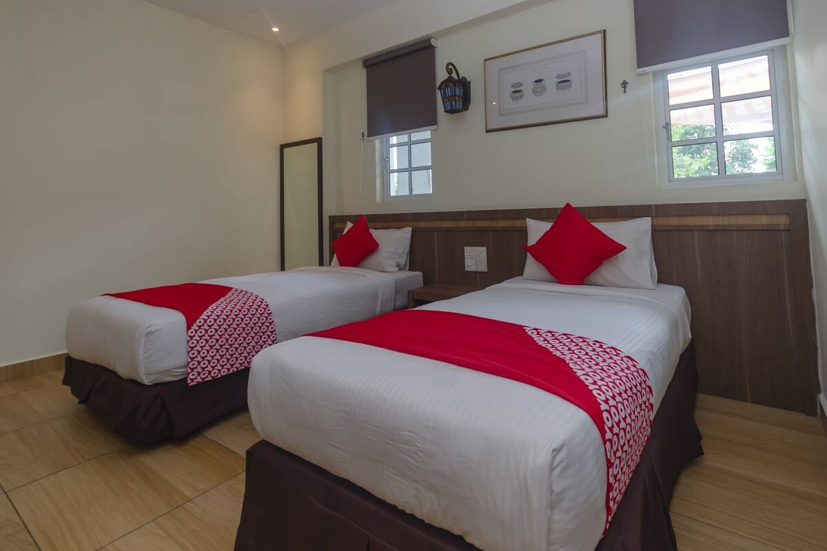 Habitación de hotel con dos camas, cada una con ropa blanca y detalles rojos, un cabecero de madera, una ventana con vistas y un cuadro en la pared.