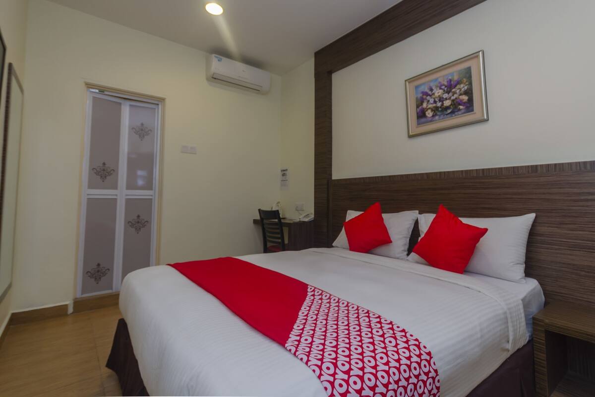 Habitación de hotel con cama, cabecera de madera, un cuadro en la pared y una puerta con panel de vidrio decorativo.