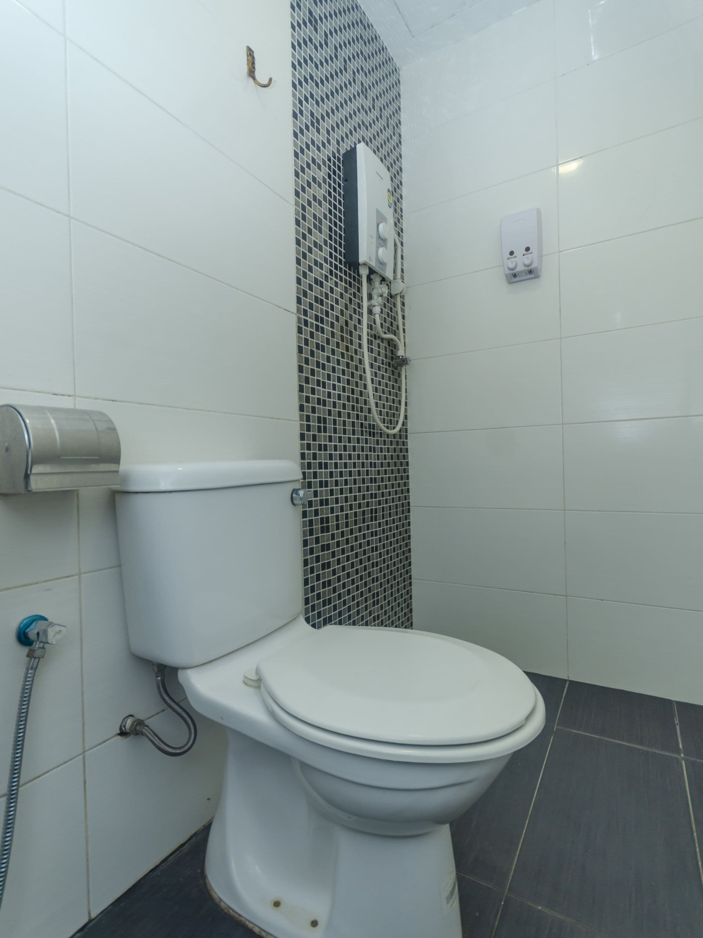 Une salle de bain avec des toilettes blanches, une douche avec un mur carrelé et un porte-rouleau de papier toilette.