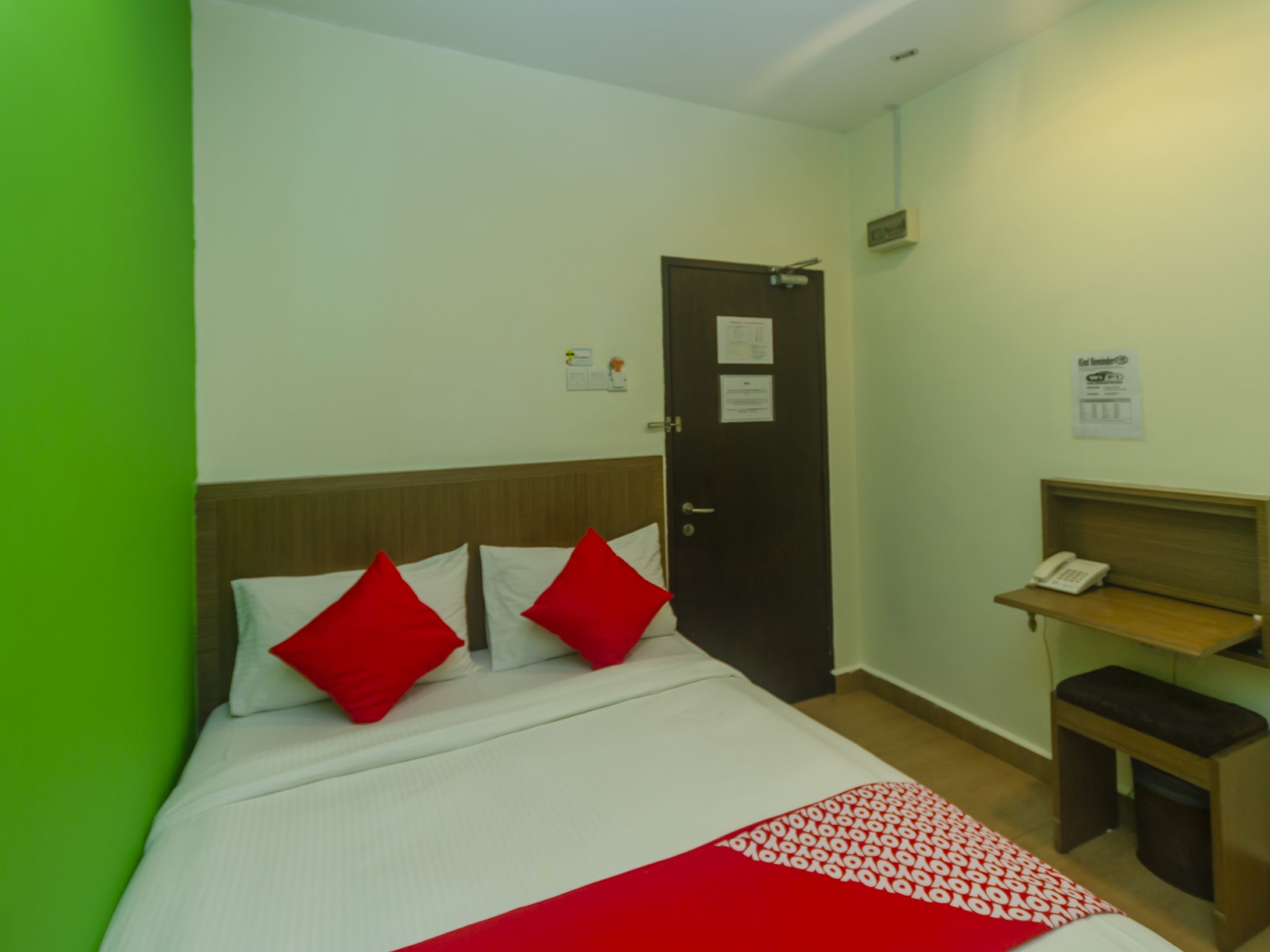 Ett hotellrum med en säng, en sänggavel i trä, ett skrivbord med en telefon och en dörr med en lapp på.