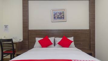 Habitación de hotel con cabecera de madera, una obra de arte floral enmarcada sobre la cama, dos almohadas rojas y una colcha con estampado rojo y blanco.