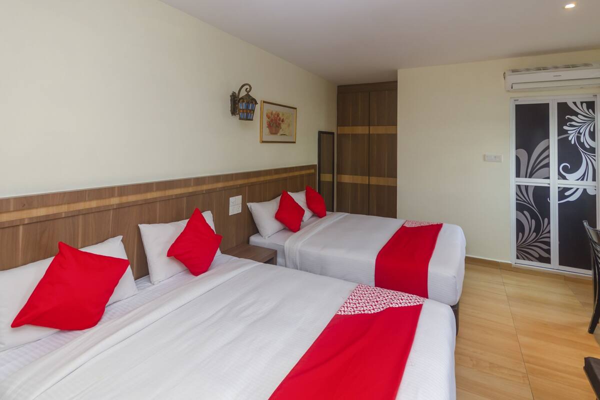 Habitación de hotel con dos camas, cada una con ropa de cama blanca y detalles en rojo, cabeceros de madera, aire acondicionado montado en la pared y una puerta con paneles de vidrio decorativos.