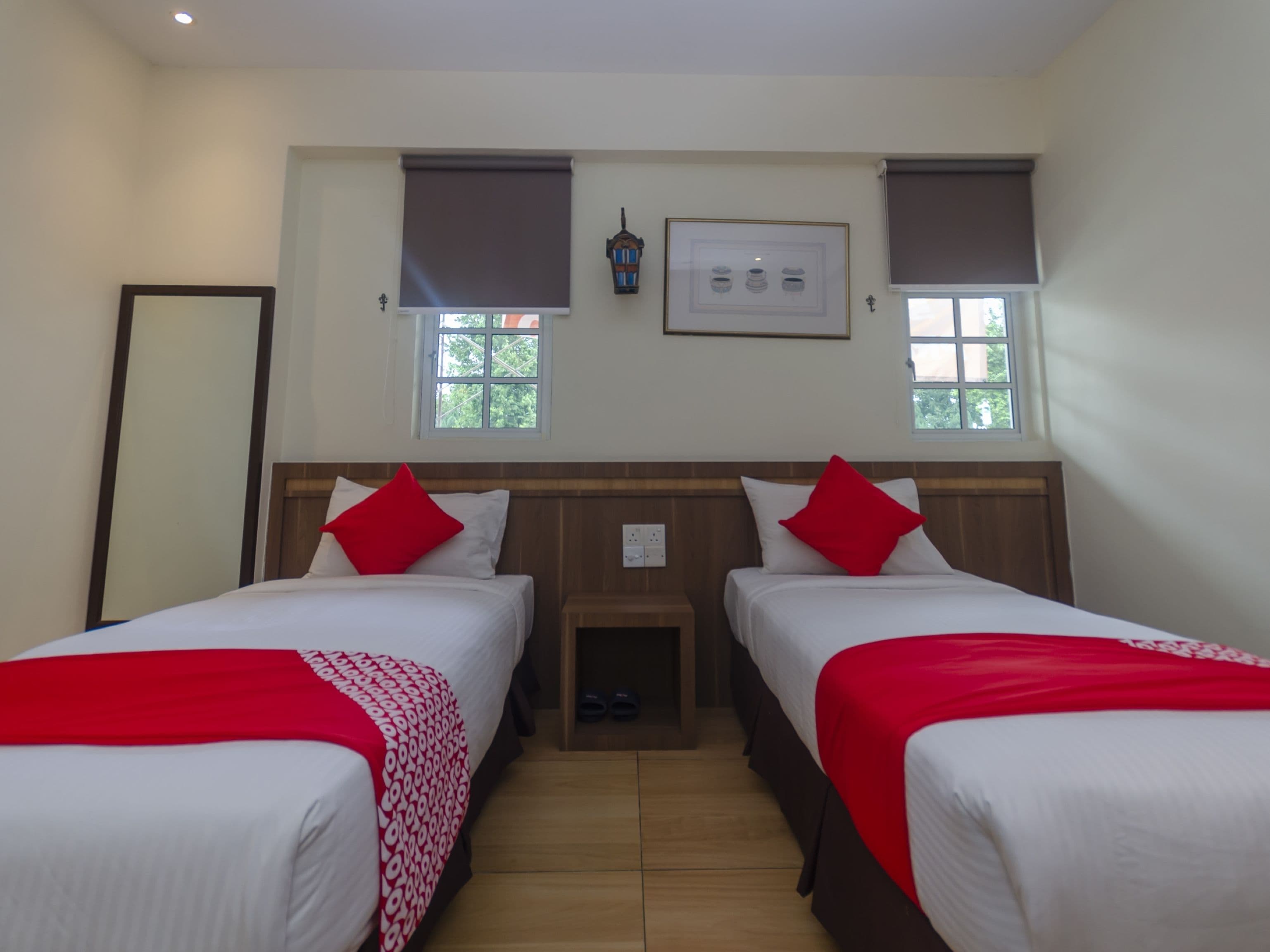 Una habitación de hotel con dos camas, cada una con una colcha roja y blanca, un cabecero de madera y una mesita de noche con una lámpara.