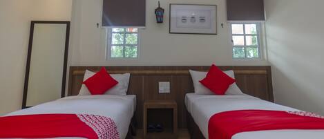 Una habitación de hotel con dos camas, cada una con una colcha roja y blanca, un cabecero de madera y una mesita de noche con una lámpara.