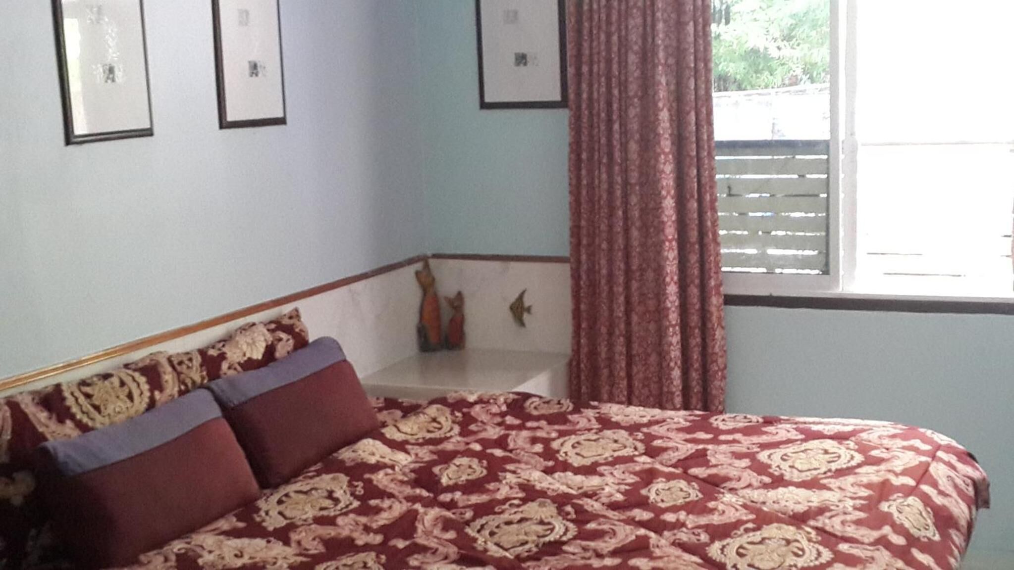 Un dormitorio con cama, ventana con cortinas y pared decorada con cuadros.