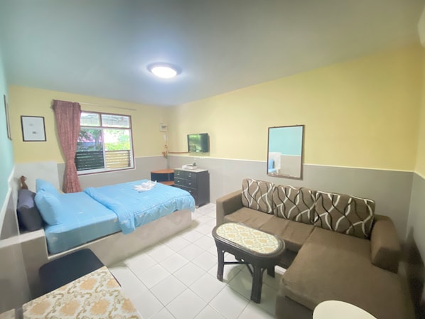 Quarto com cama, sofá, mesinha, espelho e janela com cortinas.