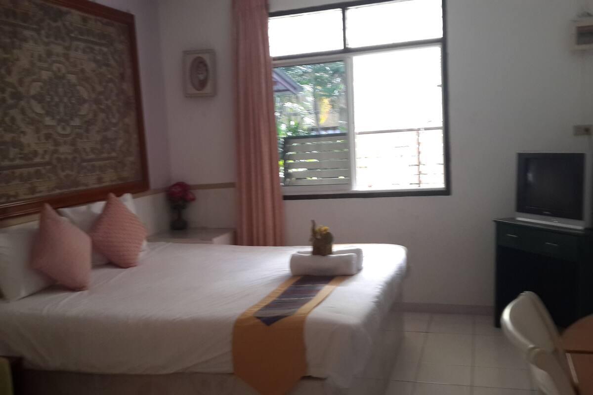 A hotel room with a bed, a television, a window with curtains, and a large painting on the wall.
