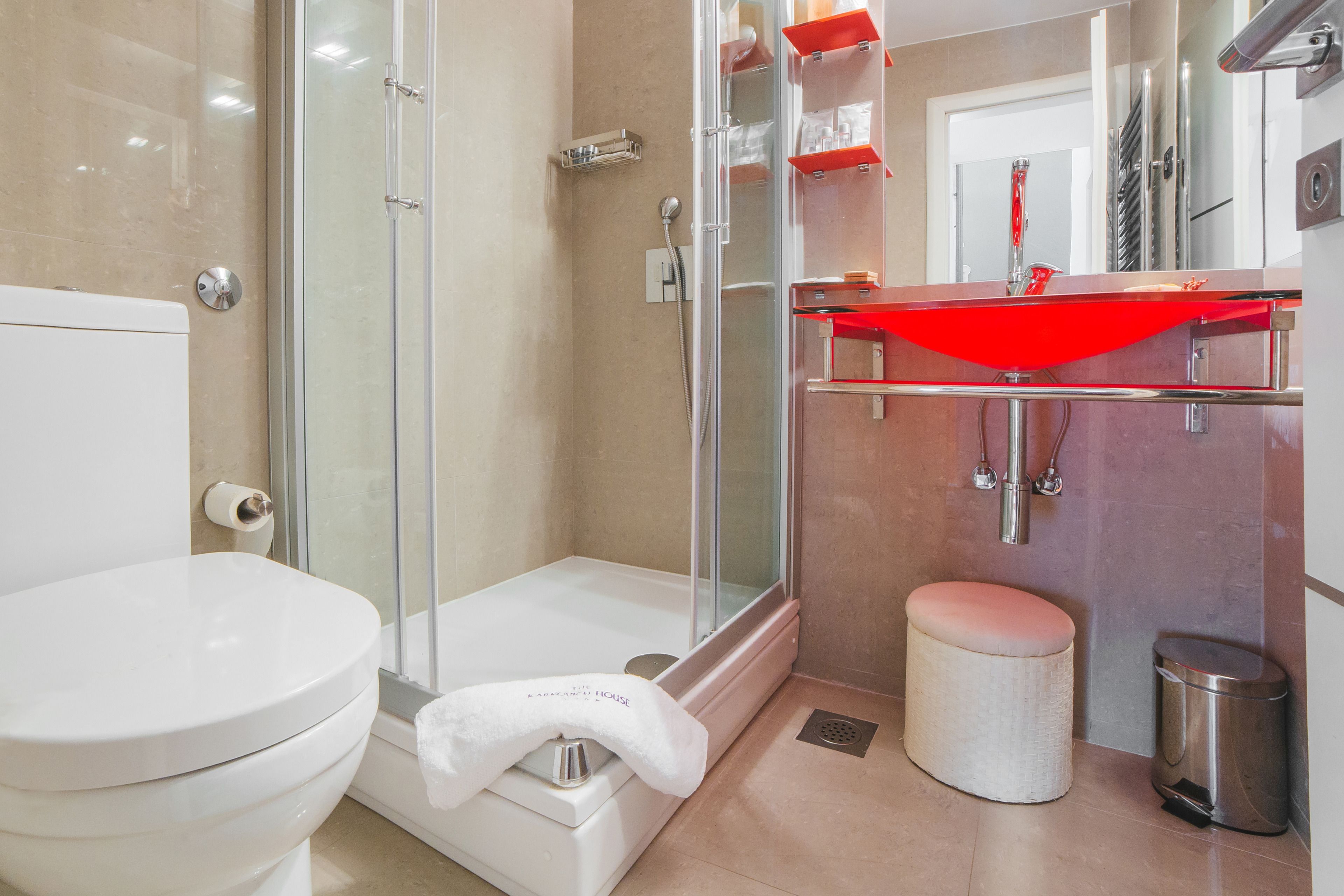 A modern bathroom with a glass shower enclosure, a white toilet, a red towel rack, and a small trash bin.