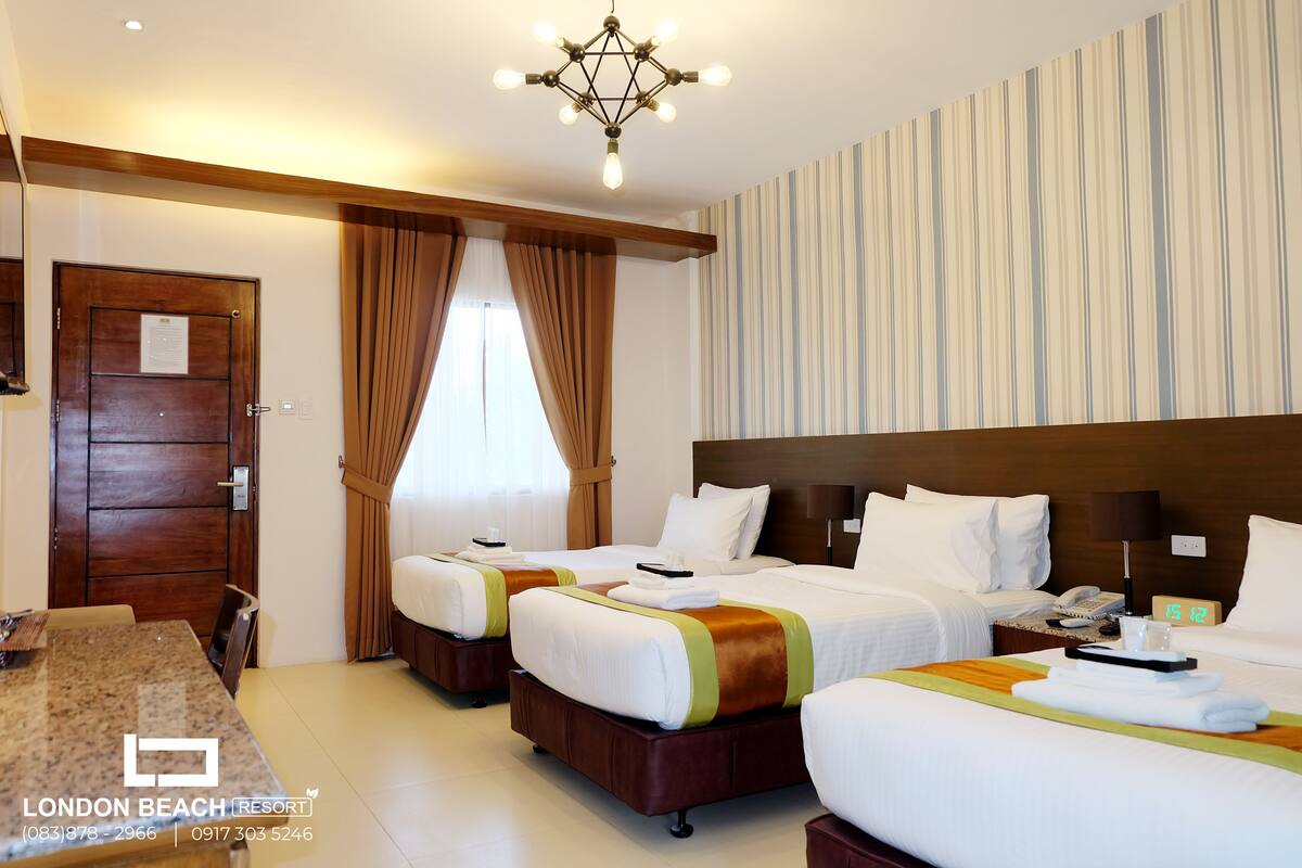 Une chambre d’hôtel avec trois lits, une porte en bois, une table à manger et un mur à rayures.