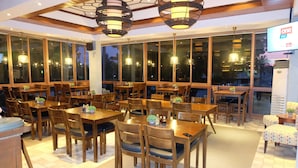 Un restaurante con mesas y sillas de madera, ventanas amplias y lámparas colgantes.