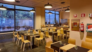 A restaurant with multiple tables and chairs, large windows, and a kitchen area.