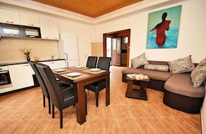 A modern kitchen with white cabinets, a dining table with chairs, and a living area with a sofa and a painting.
