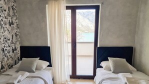 A hotel room with two beds, a view of mountains through a glass door, and a patterned curtain. - Step to Kotor bay Stoliv (Donji Stoliv)