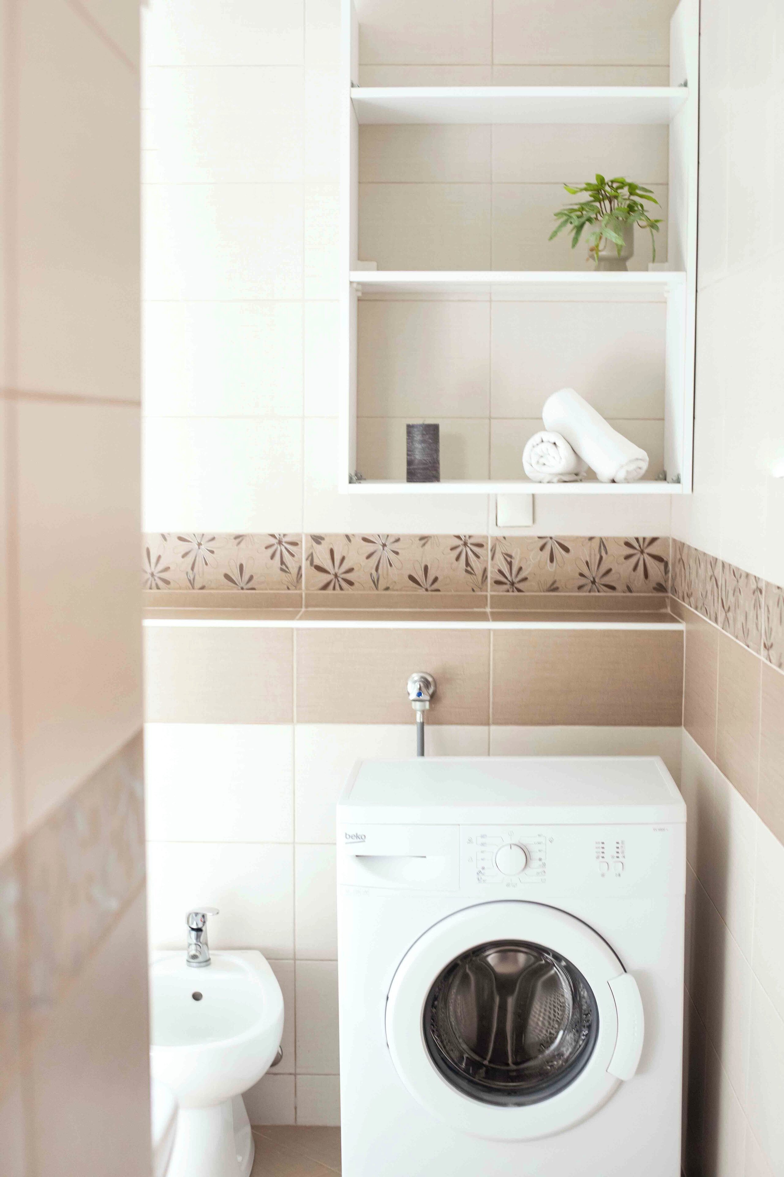 Un baño pequeño con lavadora, un lavabo y una estantería con toallas y una planta.