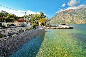A waterfront property with a stone wall, clear water, a dock, and a mountain in the background.