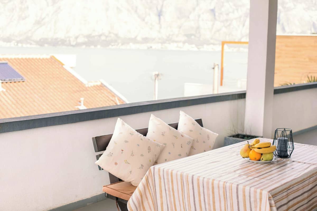 A balcony with a table, pillows, and a fruit bowl.