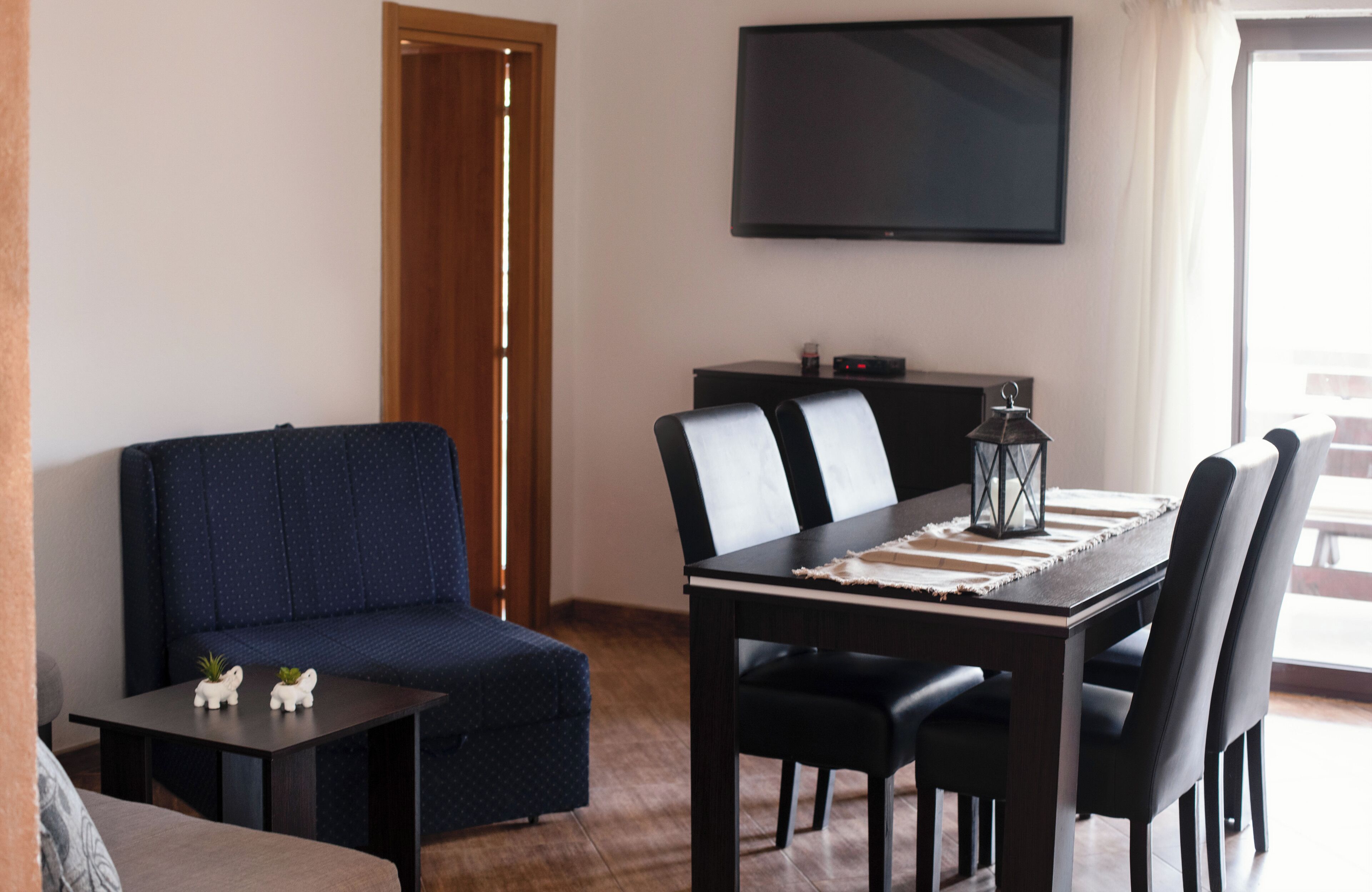 Una sala de estar con un sofá, una mesa de comedor con sillas, un televisor de pantalla plana montado en la pared y una mesita con adornos.